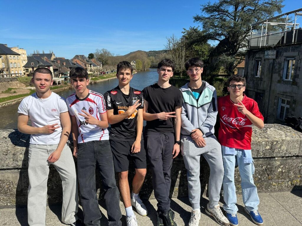 Grupo de seis estudiantes del Colegio Jaby posando sobre un puente antiguo con un río y un pueblo pintoresco al fondo en Francia.