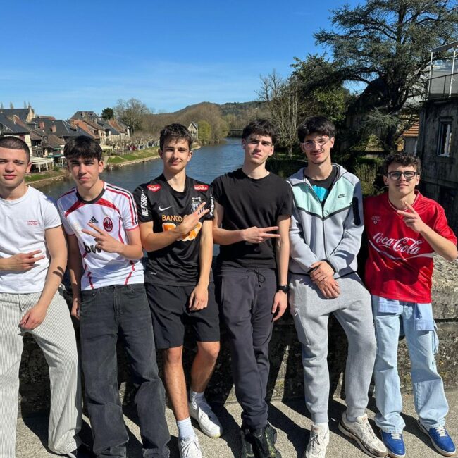 Grupo de seis estudiantes del Colegio Jaby posando sobre un puente antiguo con un río y un pueblo pintoresco al fondo en Francia.